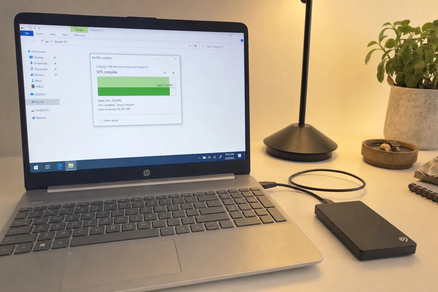 HP laptop showing Windows file copy dialog at 92 percent complete transferring 1246 items to Seagate external hard drive connected via USB cable on desk